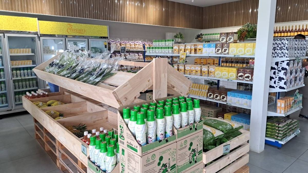 ภายในร้านจำหน่ายสินค้าชุมชนและผลิตภัณฑ์ท้องถิ่น มีลังไม้วางผักและขวดผลิตภัณฑ์ ตู้แช่ และชั้นวางสินค้า