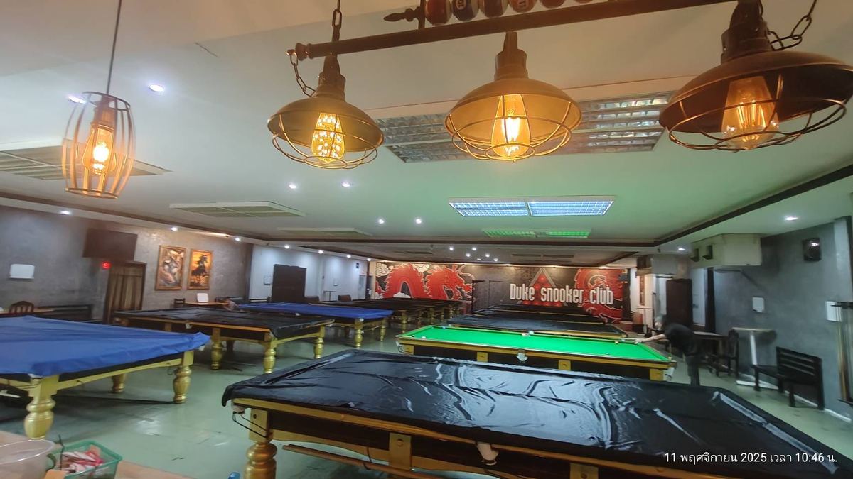 ภายใน Duke Snooker Club มีโต๊ะสนุกเกอร์หลายโต๊ะใต้โคมไฟ และป้ายชื่อร้านบนผนังด้านหลัง