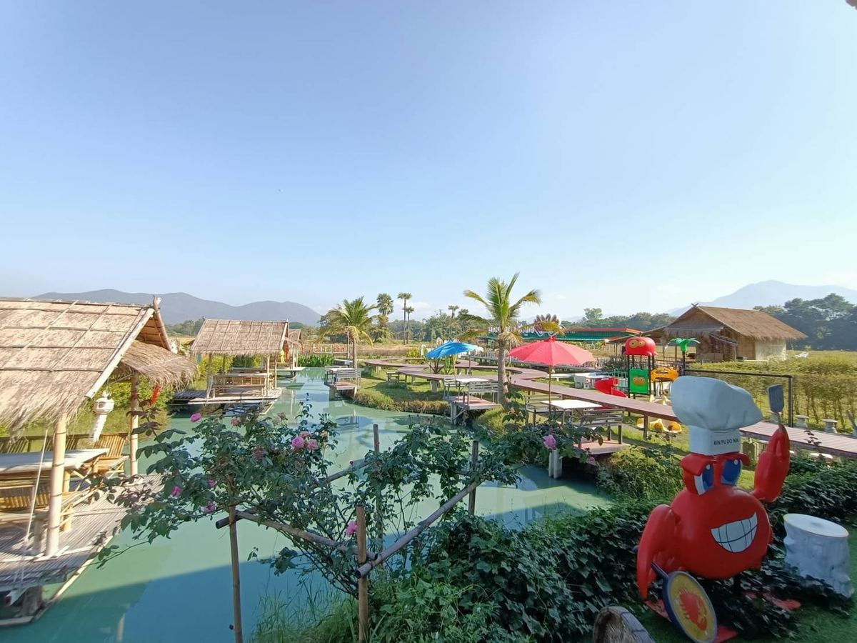 สวนของร้าน Kin Pu Do Na มีบ่อน้ำ ศาลาหลังคาจาก ร่มหลากสี และตุ๊กตาปูสีแดง