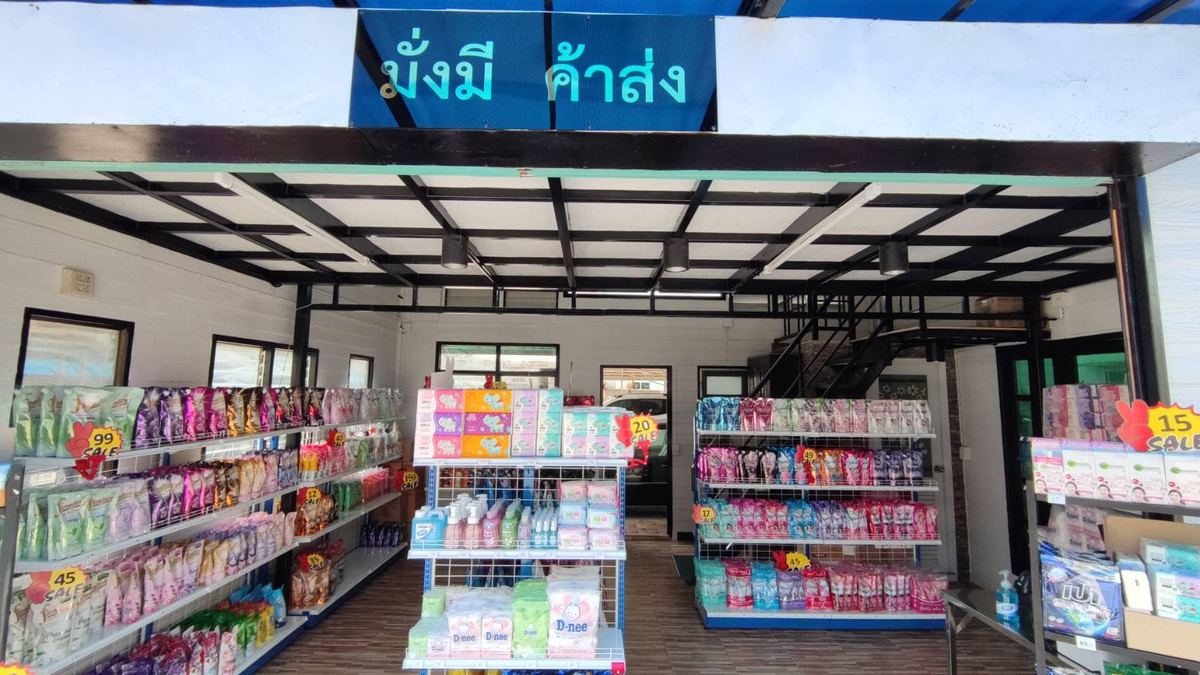 หน้าร้านมั่งมีค้าส่ง ป้ายชื่อสีฟ้า ชั้นวางน้ำยาซักผ้าและของใช้ในบ้าน