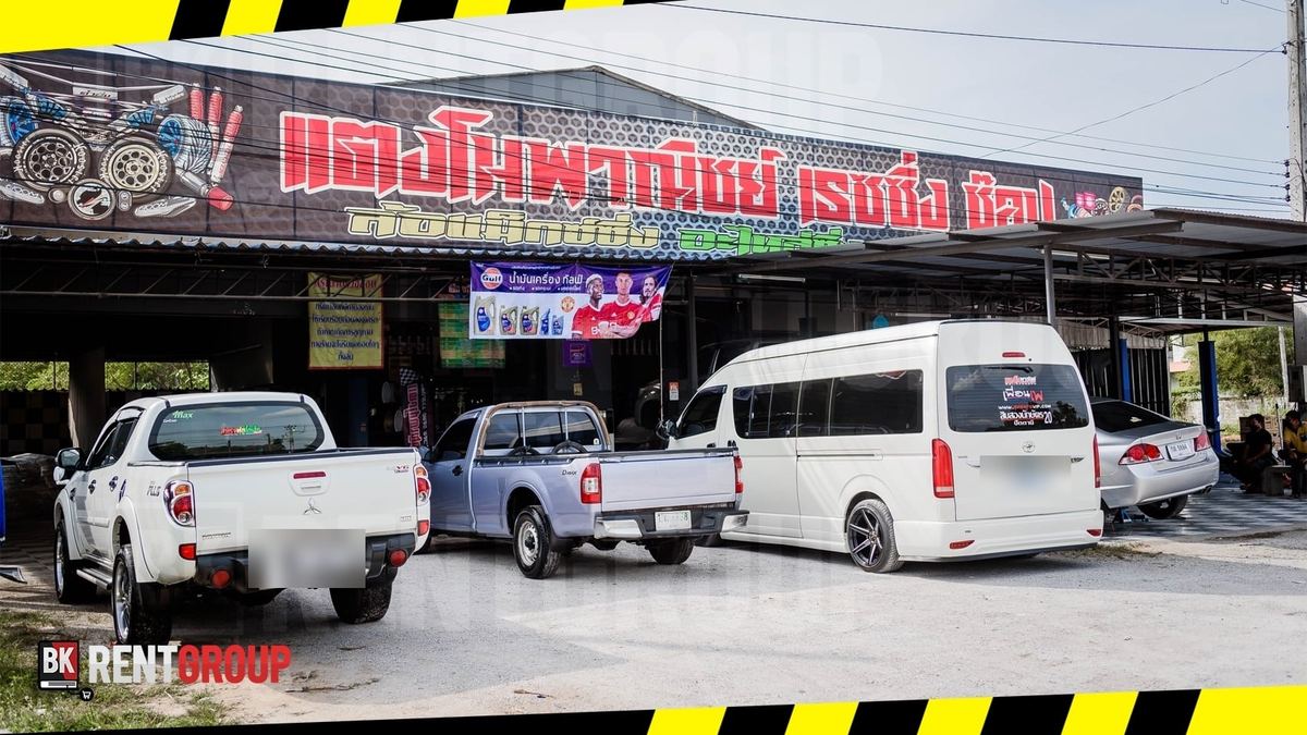 หน้าร้านแตงโมพาณิชย์ เรซซิ่ง ช็อป ป้ายสีแดงบนหลังคา รถกระบะและรถตู้จอดหน้าร้าน